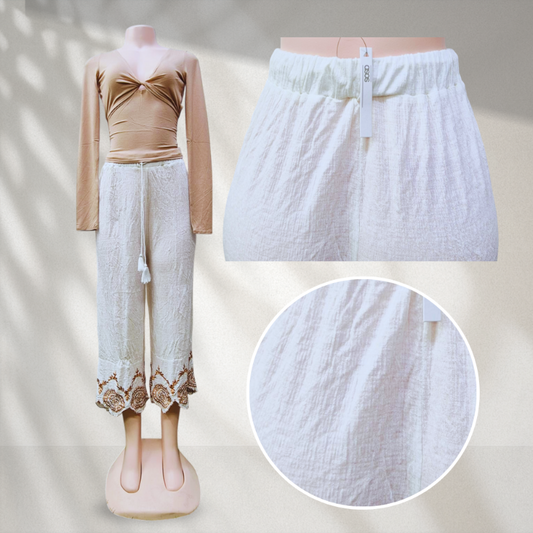 Mannequin wearing a beige top and white pants with lace details, on a neutral background.